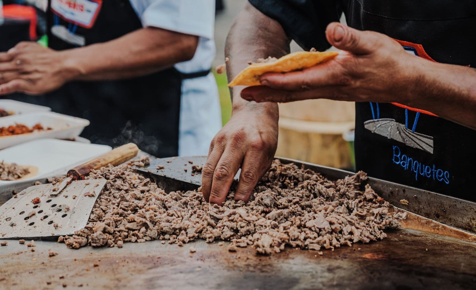 Taquero sirviendo carne asada en una plancha humeante